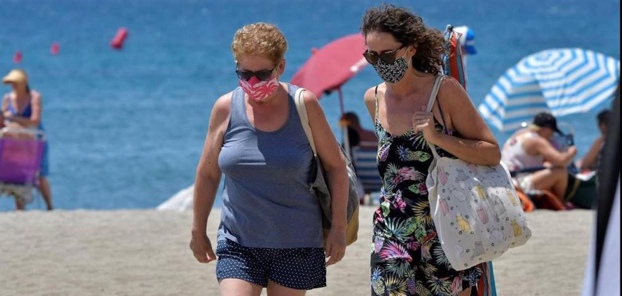 Dos mujeres con mascarilla en la playa en un día de mucho calor / EFE