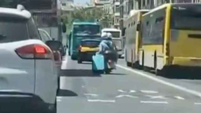 Un pasajero de una motocicleta arrastra una maleta por el centro de Barcelona / INSTAGRAM