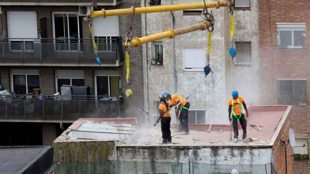 Tres operarios, colgados de una grúa, trabajan este lunes en el tejado de uno de los bloques afectados / EFE