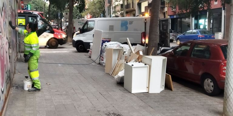 Una operaria limpia unos grafitis junto a unos muebles dejados en una acera / METRÓPOLI - JORDI SUBIRANA