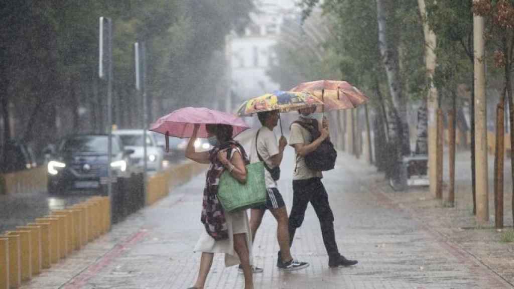 Una mujer y dos jóvenes pasean bajo la lluvia con paraguas en Barcelona