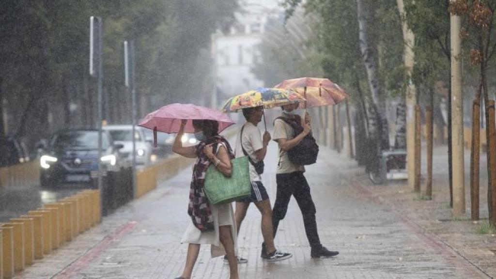 Una mujer y dos jóvenes se resguardan de la lluvia con un paraguas en Barcelona