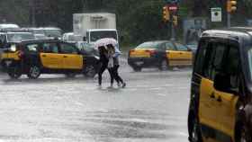 Dos mujeres cruzan una calle durante un episodio de lluvias y frío posterior a días con clima veraniego en Barcelona