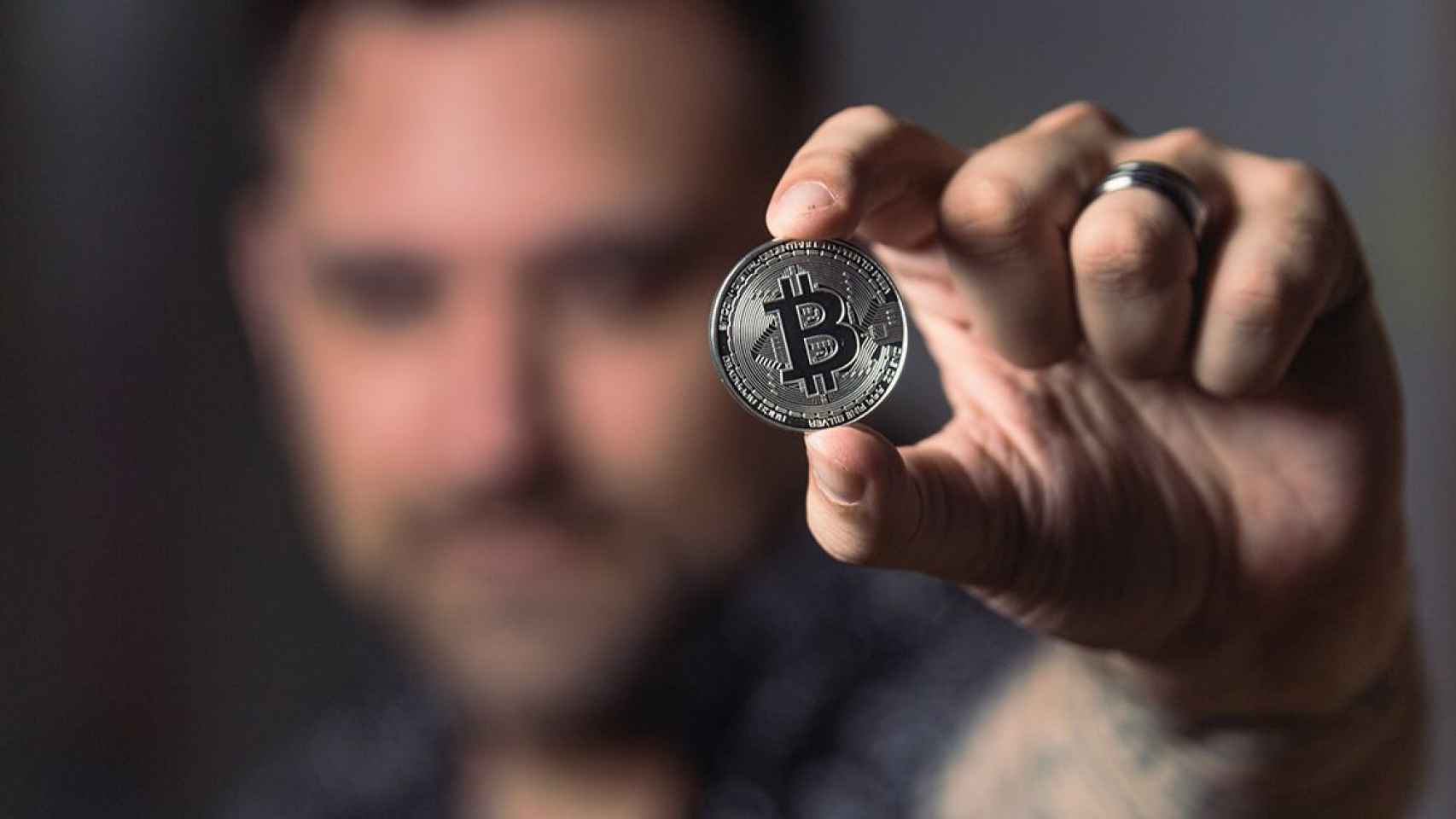 Hombre muestra una moneda con el logo de Bitcoin / PEXELS