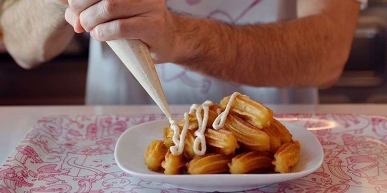 Camarero de Comaxurros añadiendo una salsa a una ración de churros / INSTAGRAM