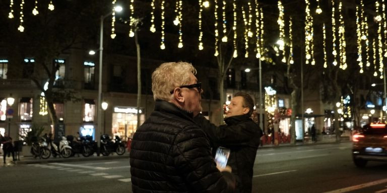 Un hombre hace fotos a las luces de Navidad del paseo de Gràcia mientras otro camina por debajo / PABLO MIRANZO - MA