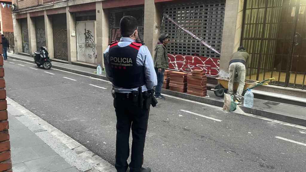 Un mosso d'esquadra observa a dos trabajadores tapiando uno de los locales / MOSSOS D'ESQUADRA