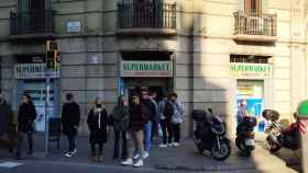 Un grupo de jóvenes delante de un pequeño 'super' del Eixample / METRÓPOLI