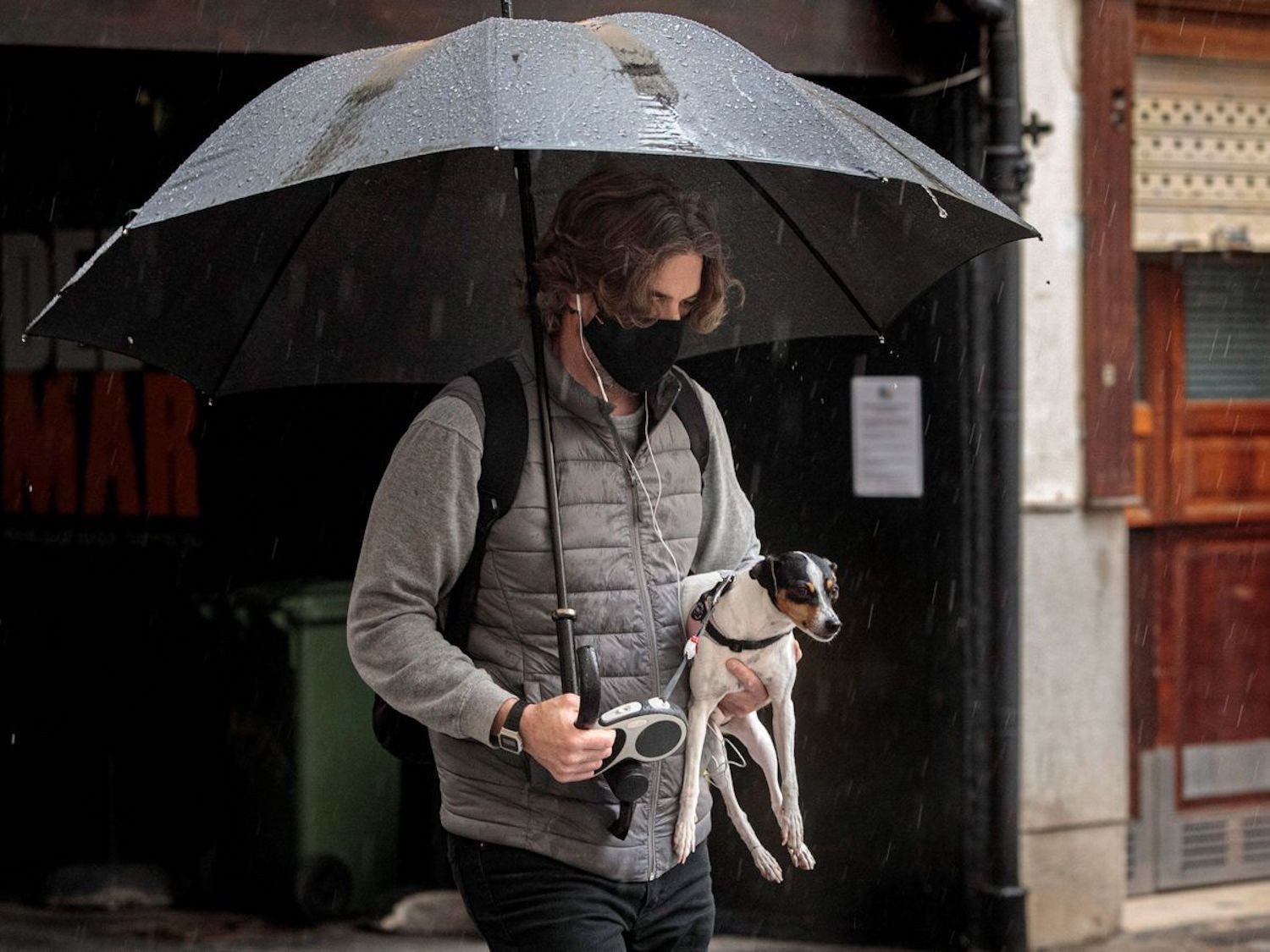 Un joven y su perro se protegen de la lluvia bajo un paraguas / EFE