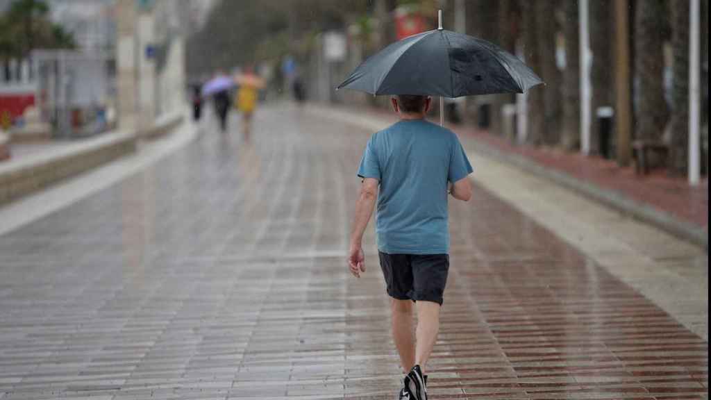 Una persona en el paseo marítimo cubierto con un paraguas / EFE