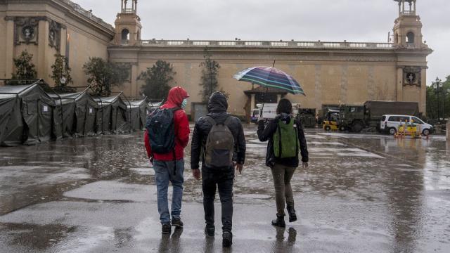 Tres jóvenes pasean bajo la lluvia en la zona de las fuentes de Montjuïc de Barcelona