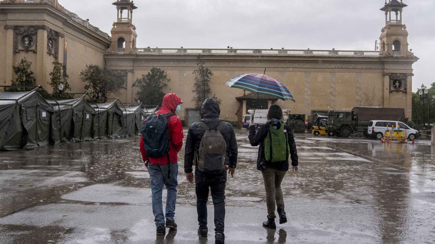 Tres jóvenes pasean bajo la lluvia en la zona de las fuentes de Montjuïc de Barcelona