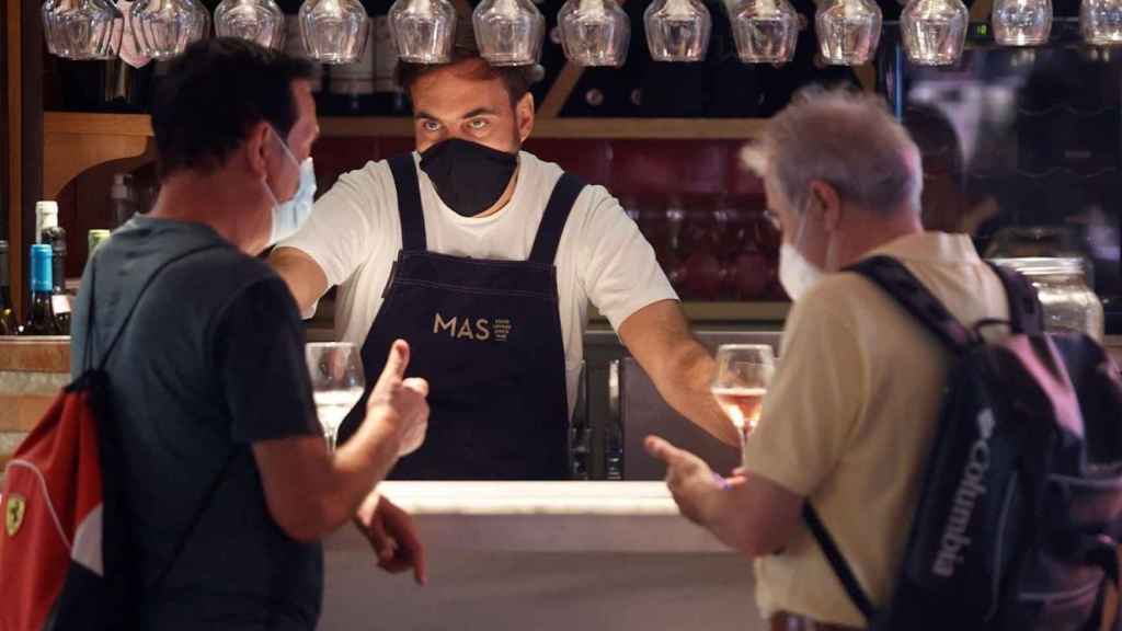 Un camarero y dos clientes con la mascarilla en el interior de un bar / EFE