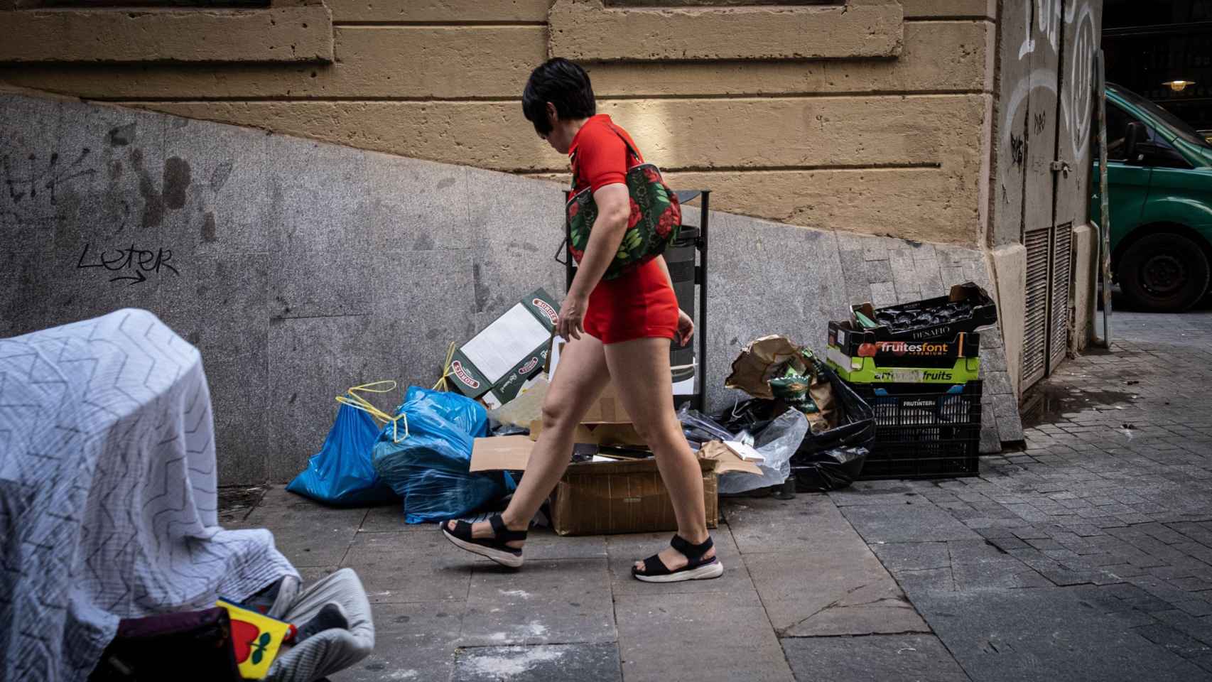 Una residente del Raval pasea por delante de una montaña de basura a pie de calle que sufren los vecinos / PABLO MIRANZO - MA