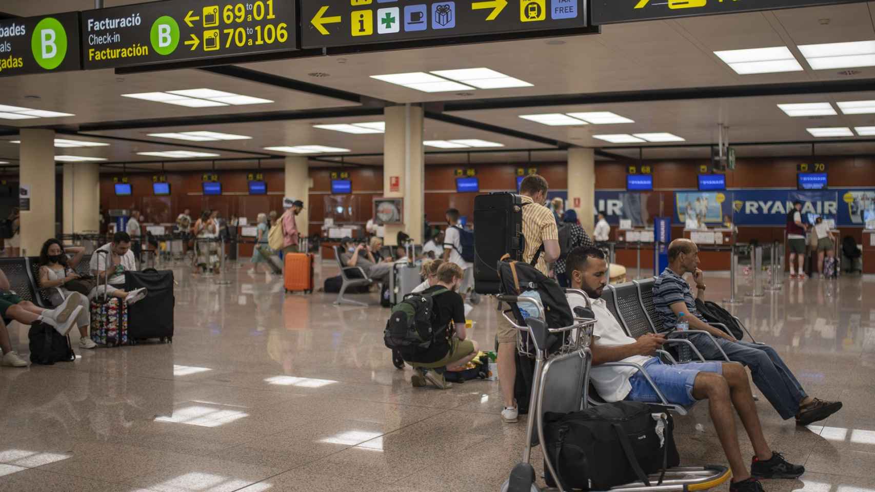 Varias personas esperan sentadas con sus maletas en el Aeropuerto Josep Tarradellas Barcelona-El Prat / EUROPA PRESS