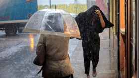 Dos personas se resguardan del temporal de lluvia / EFE