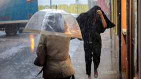 Dos personas se resguardan de un temporal de lluvia / EFE