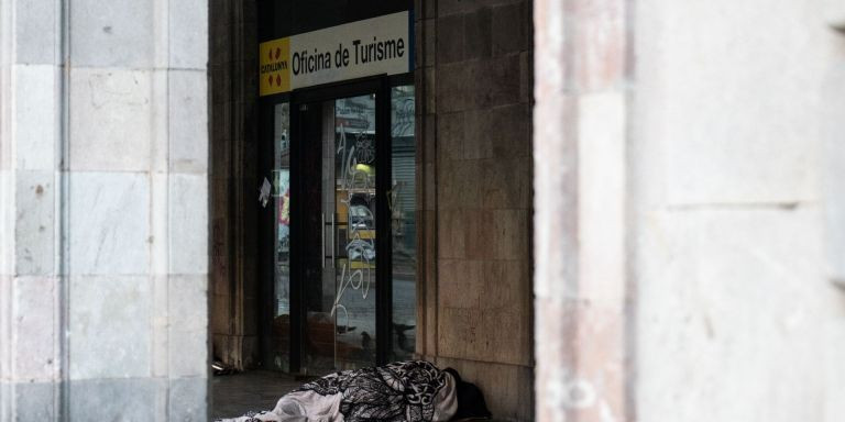Una persona sintecho duerme al lado de una oficina de turismo en La Rambla / GALA ESPÍN - METRÓPOLI
