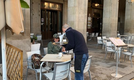 Un camarero sirve un café a una clienta en una terraza de la plaza Reial del barrio Gòtic / V.M.