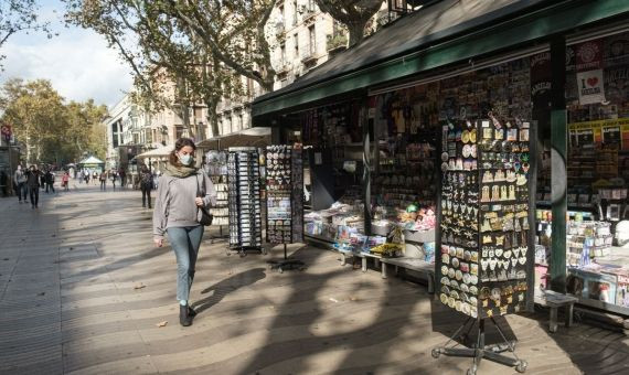 Una mujer camina delante de un kiosko en La Rambla, casi vacía por la ausencia de turistas / CG- PABLO MIRANZO