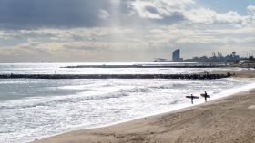 Dos surfistas en la playa de Mar Bella, en Barcelona, con la Barceloneta de fondo