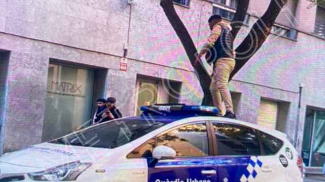 Un joven subido encima de un coche policial de la Guardia Urbana en la calle de Sant Oleguer, en las inmediaciones de la comisaría de la calle de Tàpies