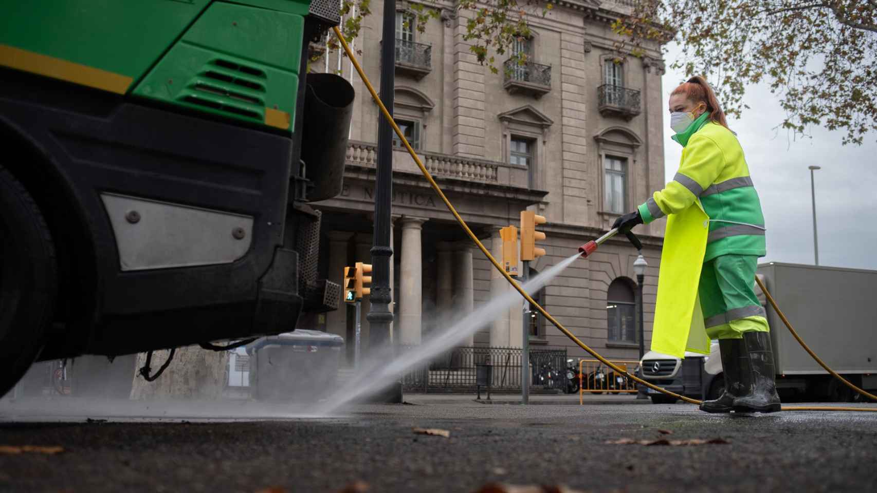 Una trabajadora riega una calle con una manguera en enero en Barcelona