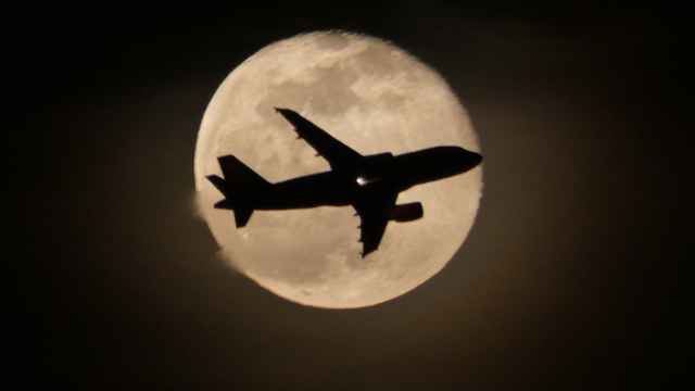 Un avión atravesando la luna llena vista desde la playa de Gavà