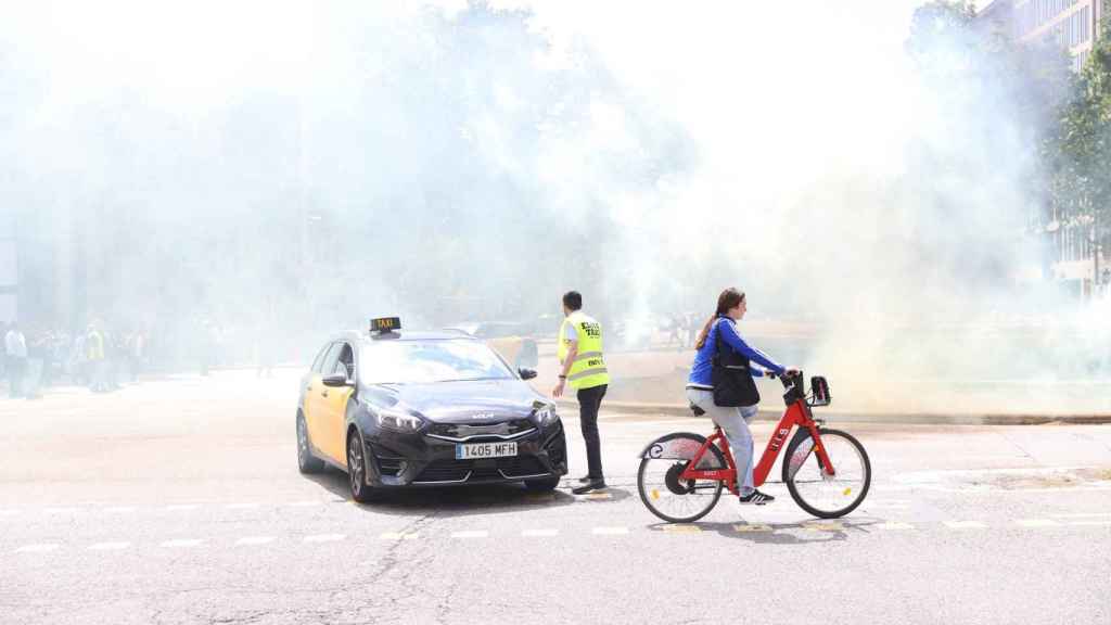 Un taxi y una bicicleta entre humo en la protesta de taxistas