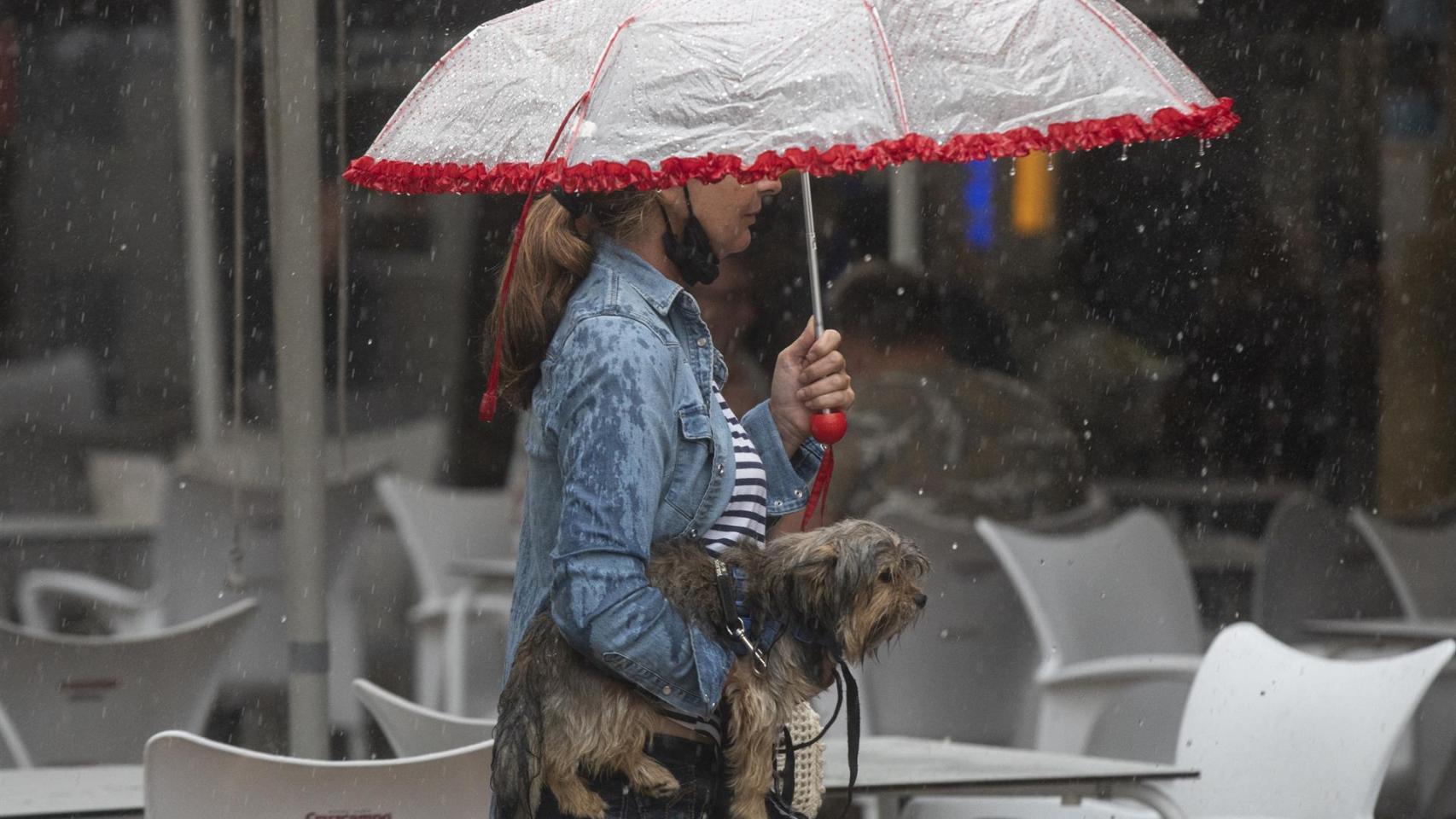 Una mujer lleva a su perro en brazos bajo una tormenta en Barcelona