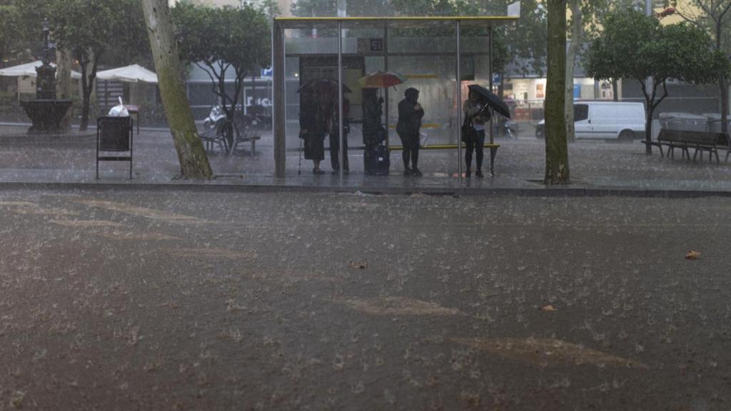 Varias personas esperan en la parada del bus durante la tormenta en Barcelona