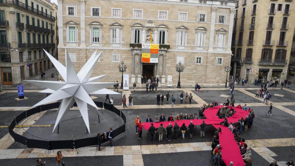 Un tapiz y un lazo memorial del SIDA de despliegan en las fachadas del Ayuntamiento, Palau de la Generalitat y plaza Sant Jaume, este domingo en el que se celebra el Día Mundial del Sida