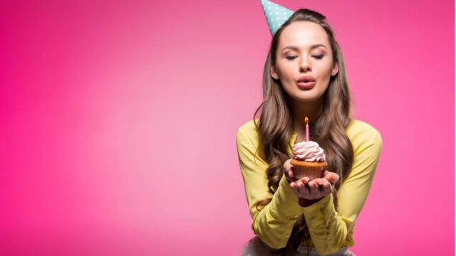 Mujer con sombrero de fiesta sosteniendo cupcake y soplando vela