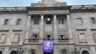El alcalde Jaume Collboni, representantes del gobierno, de grupos políticos y de entidades han desplegado una pancarta en el balcón del Ayuntamiento con el lema de este año para el 8M 'Trenquem la precarietat'