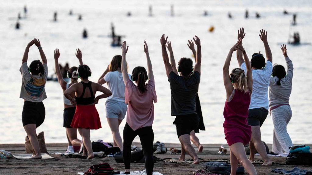 Expats practicando yoga en la playa de la Barceloneta al amanecer